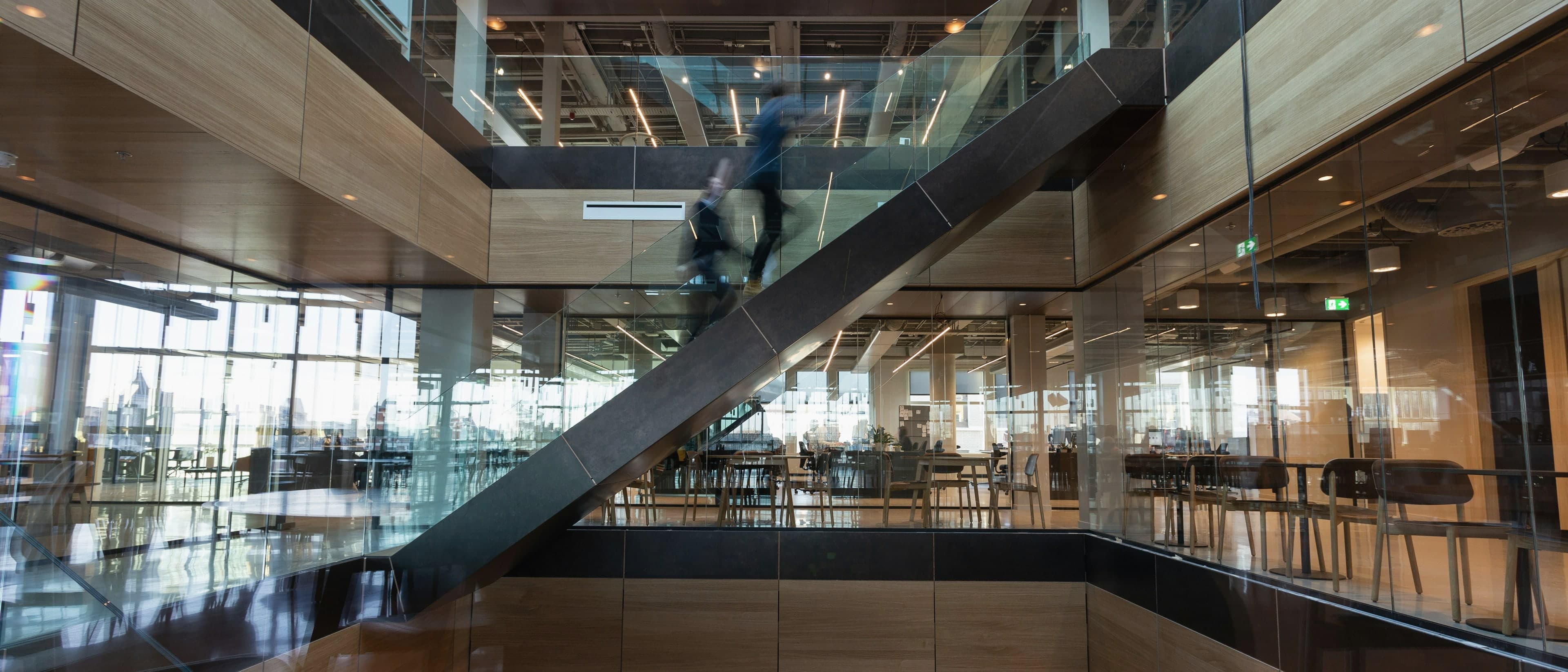 Offenes Atrium eines Bürogebäudes aus Eichenholz und Glas, zwei Menschen gehen die Treppe hinauf