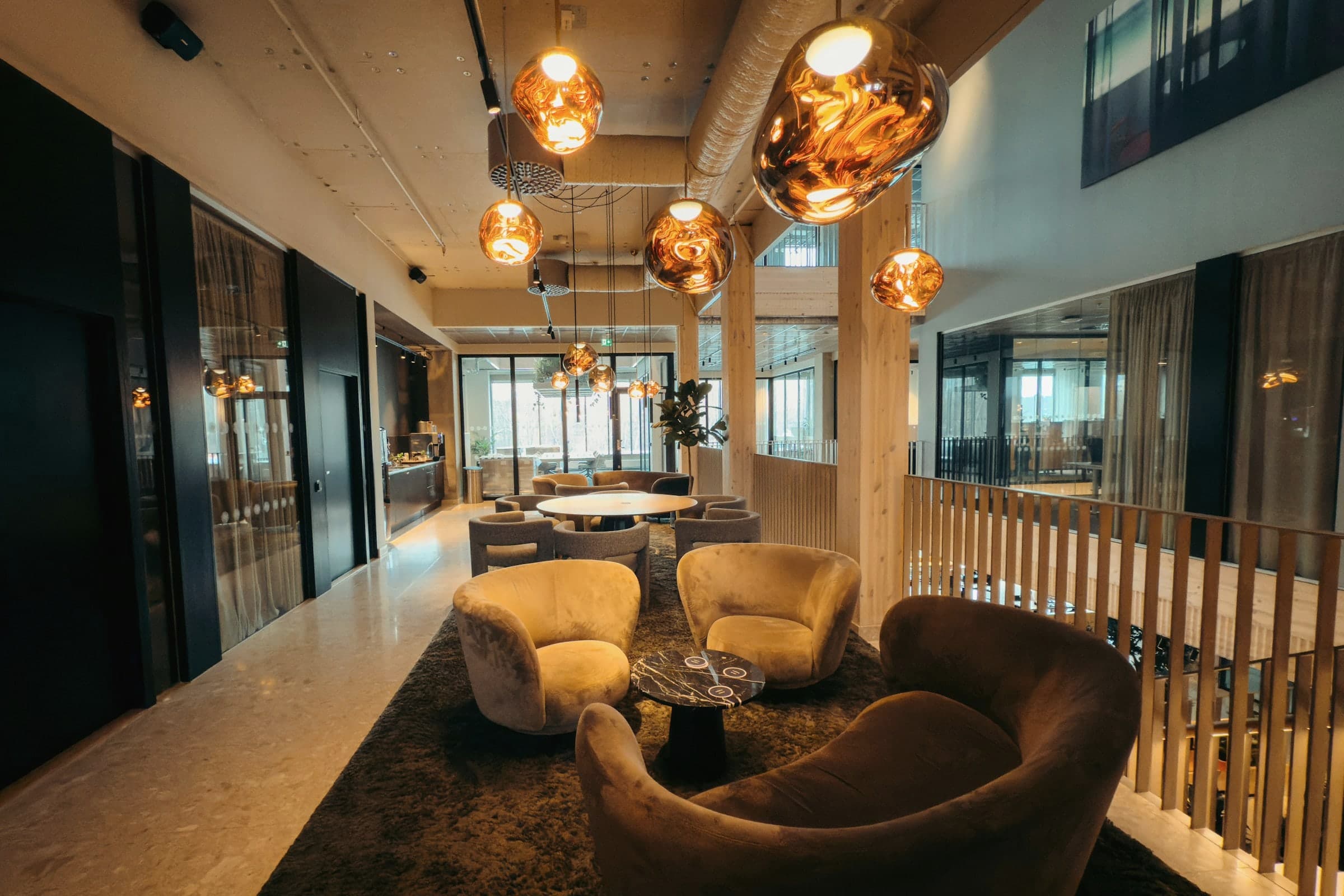 Lounge in einem Bürogebäude mit Samtsesseln, Marmortisch, Teppich und goldenen Pendelleuchten